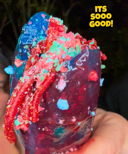 Colorful pickle with red, blue, and green toppings cotton candy crunch held by a person.